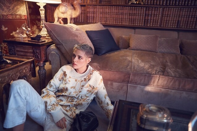 在 Coco Chanel 米褐色麂皮梳化旁邊，穿著 Chanel 繡花針織衫、棉質長褲、皮背包。