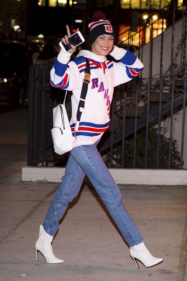 Bella Hadid 以衛衣配上牛仔褲雖是普通不過的街頭造型，加上同色系的白色高跟短靴及皮革背囊