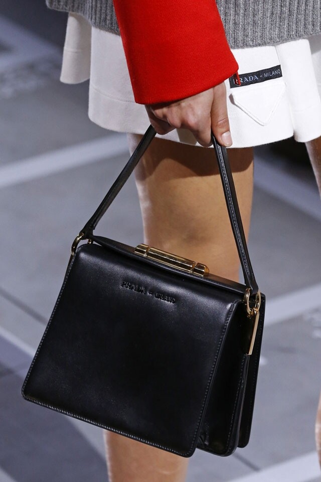 Prada 的手袋形狀端正，以黑色皮革配上金屬飾扣，顯得份外典雅。